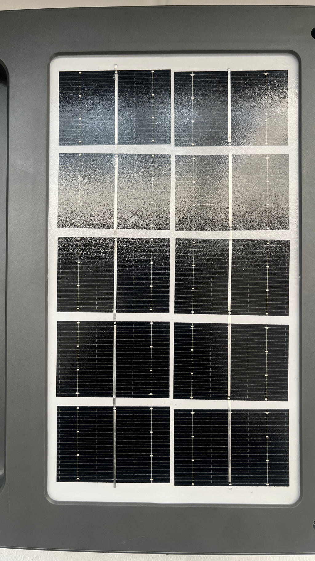 A rectangular solar panel with multiple dark photovoltaic cells separated by white grid lines, mounted on a dark gray housing.