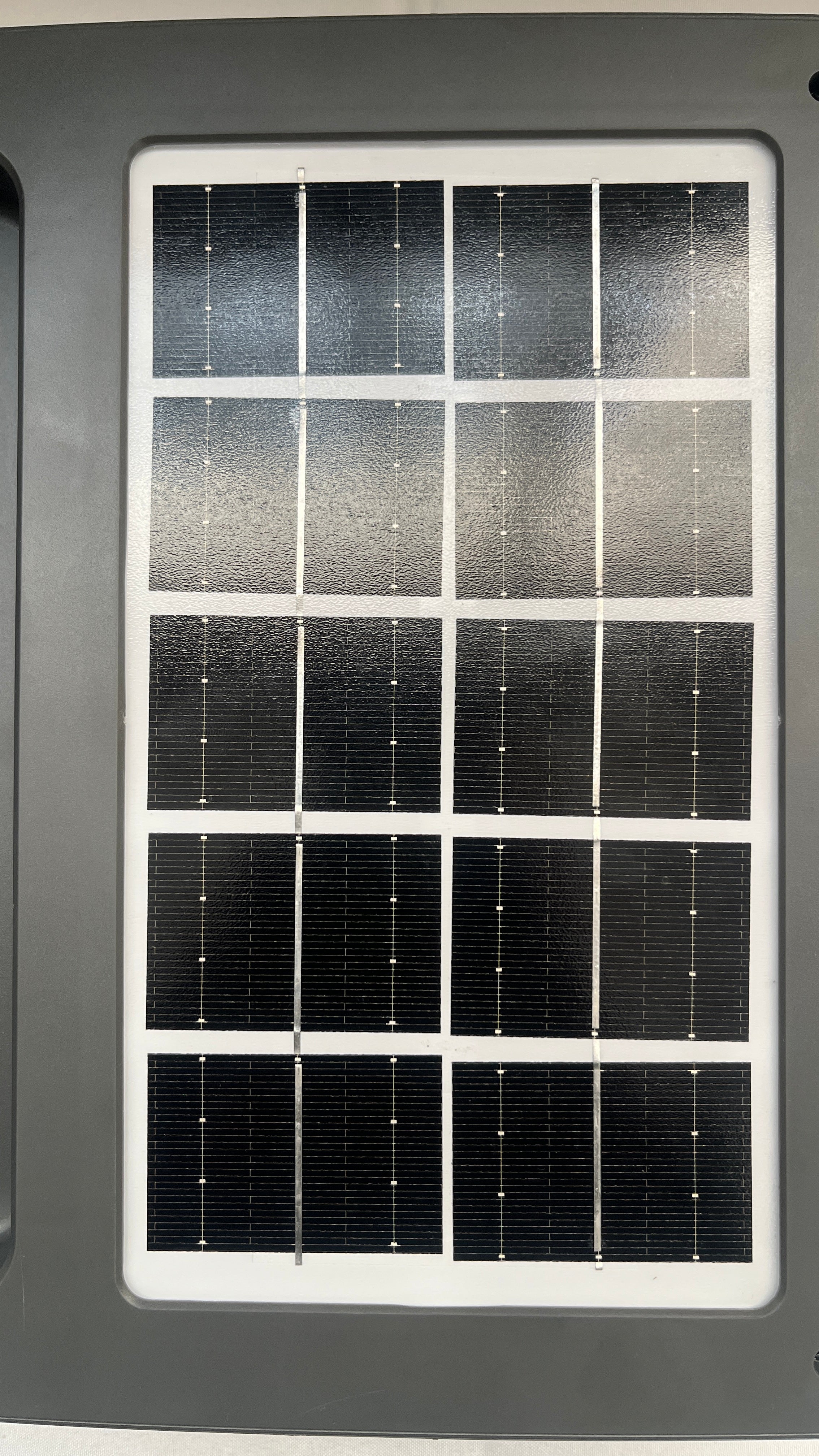 A rectangular solar panel with multiple dark photovoltaic cells separated by white grid lines, mounted on a dark gray housing.