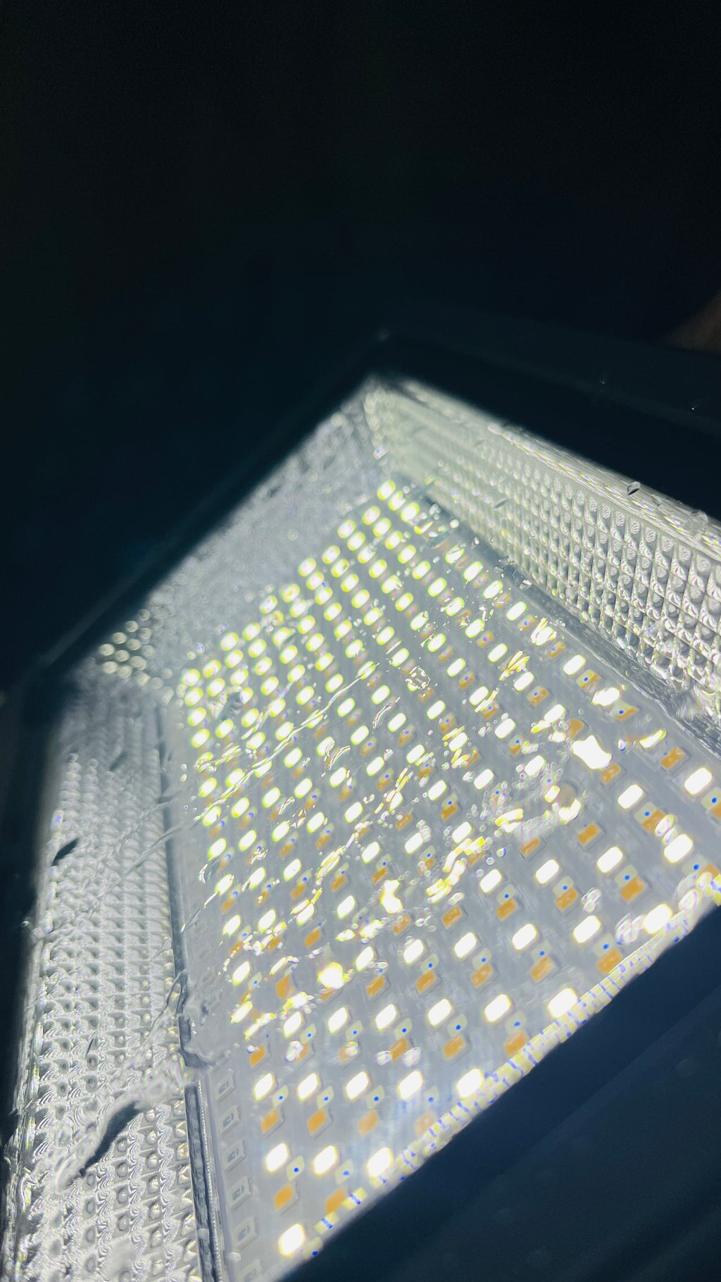 A close-up view of a square LED light panel with many small illuminated white LEDs on a reflective silver surface, set against a dark background.