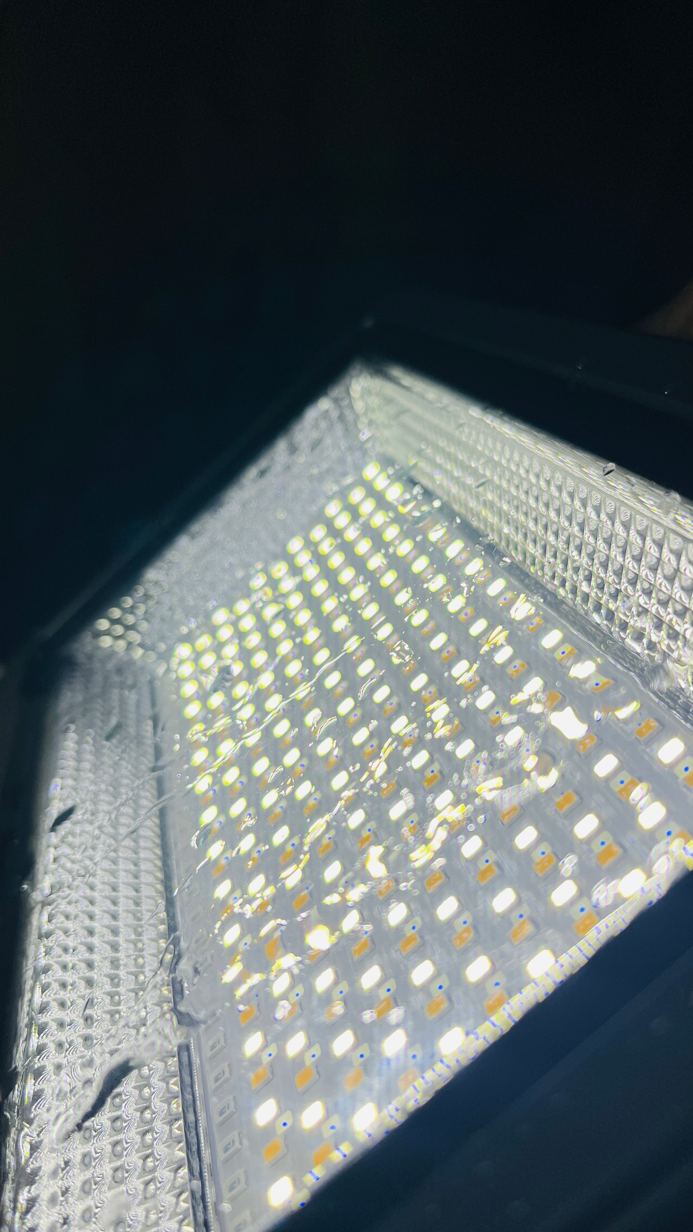 A close-up view of a square LED light panel with many small illuminated white LEDs on a reflective silver surface, set against a dark background.